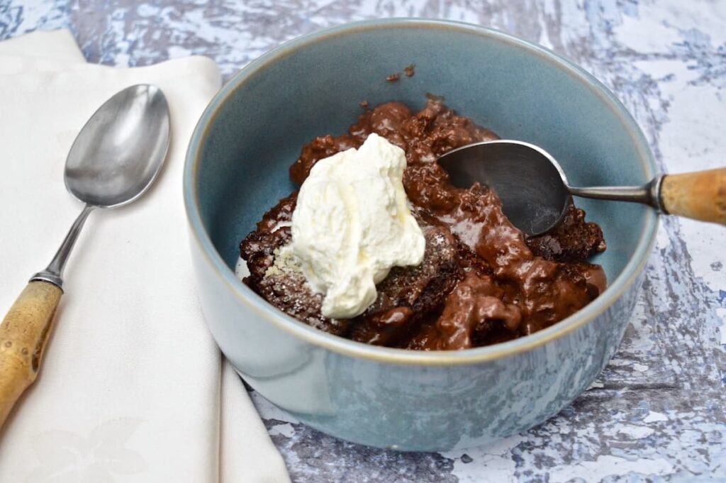 A blue bowl of self-saucing chocolate pudding with cream.