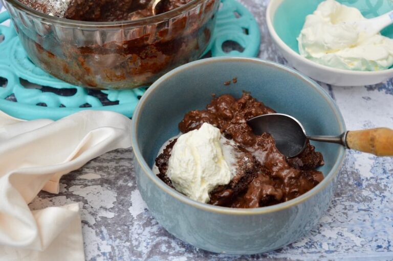 A blue bowl of self-saucing chocolate pudding with cream.