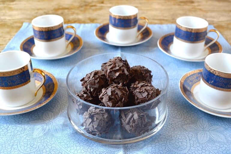 A glass bowl of whisky truffles covered in dark chocolate flakes. Also five Turkish coffee cups with a blue and gold stripe.