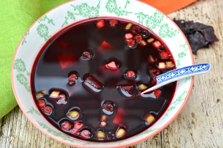 Bowl of beetroot miso soup with tofu and chopped spring onions and inserted spoon.