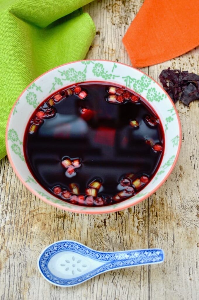 A bowl of beetroot miso soup with tofu and chopped spring onions.