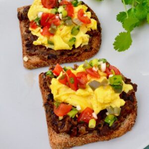 Two slices of egg and beans on toast - Mexican style. Wholemeal toast topped with black beans and scrambled eggs with pico de gallo scattered over the top.