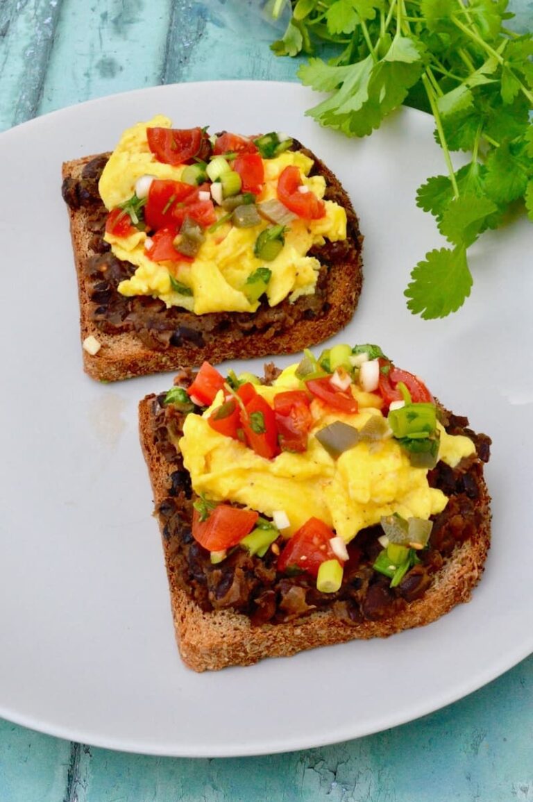 Two slices of egg and beans on toast - Mexican style. Wholemeal toast topped with black beans and scrambled eggs with pico de gallo scattered over the top.