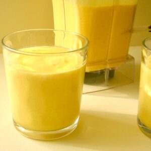 Two glasses of mango carrot smoothie with more in the blender behind.