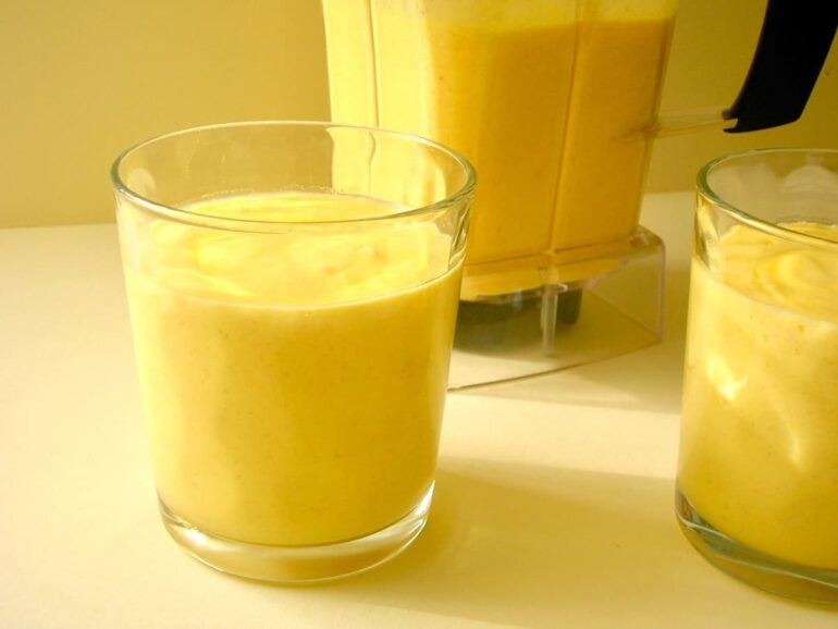 Two glasses of mango carrot smoothie with more in the blender behind.