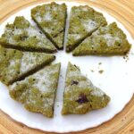Triangles of cacao nibbed matcha shortbread on a white plate with one piece missing.
