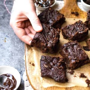 A board with vegan Christmas brownies and a hand picking up one of them.
