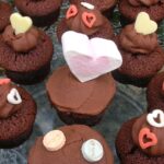 A batch of chocolate Valentine's cakes covered in whipped chocolate ganache and decorated with various edible hearts.