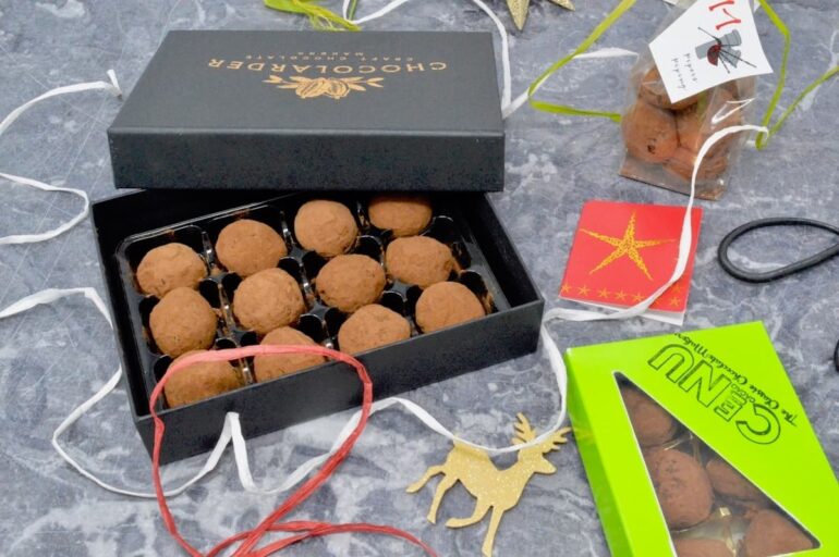 A box of homemade vegan gingerbread chocolate truffles, surrounded by gift wrapping paraphernalia.