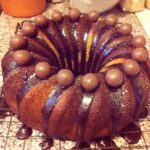 A marbled malted chocolate bundt cake topped with chocolate glaze and Maltesers on a wire rack. Dusted with edible glitter.