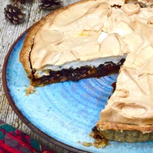 Mincemeat meringue pie sitting on a blue plate with a slice missing.