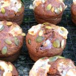 A batch of savoury pumpkin muffins with toasted goat's cheese and pumpkins seeds on top.