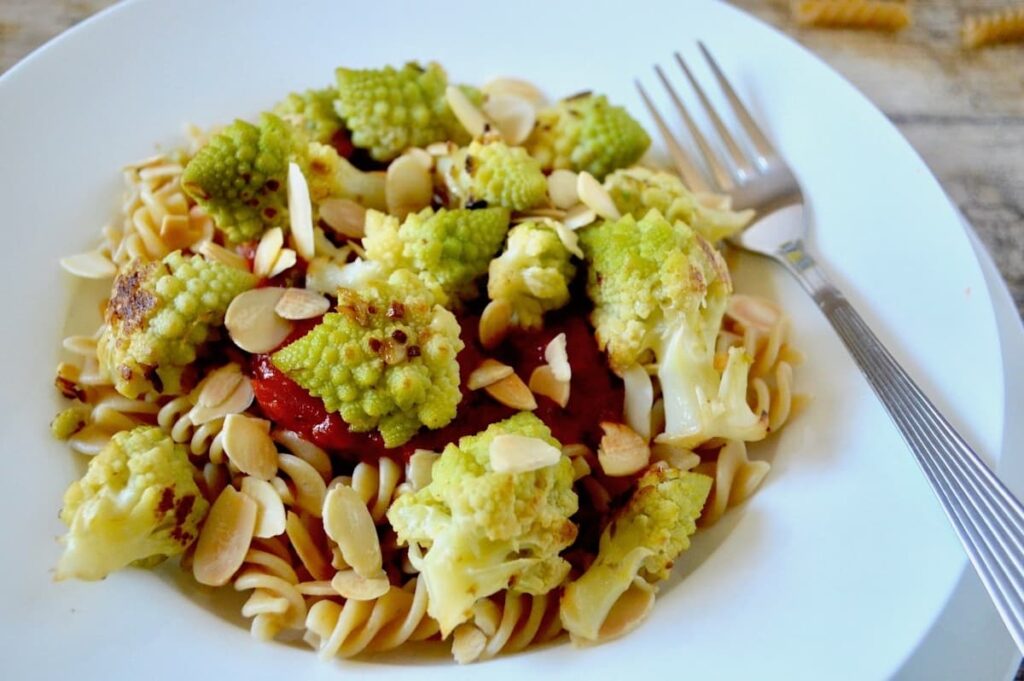 A white bowl of romanesco pasta with fork, sitting on a white plate.
