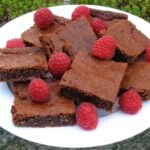 Pile of gluten-free almond toffee brownies with raspberries scattered over.