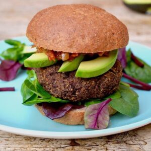 Quinoa chickpea burger in a wholemeal bun with avocado slices, tomato and onion relish and salad leaves.