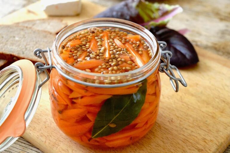 An open clip top jar of homemade quick and easy carrot pickles with salad leaves and bread in the background.