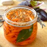 Open clip top jar of homemade quick and easy carrot pickles with salad leaves and bread in background.