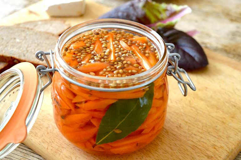 Open clip top jar of homemade quick and easy carrot pickles with salad leaves and bread in background.