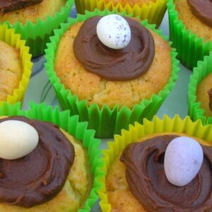 Surprise Easter egg cupcakes in bright yellow and green paper cases with a chocolate ganache nest with egg on the top.