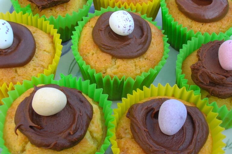Surprise Easter egg cupcakes in bright yellow and green paper cases with a chocolate ganache nest with egg on the top.