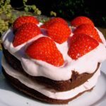A heart shaped chocolate cake sandwiched with strawberry cream and topped with sliced strawberries.