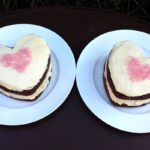 Two Valentine's chocolate heart cakes with white chocolate icing and pink sprinkles in a heart shapes on top.