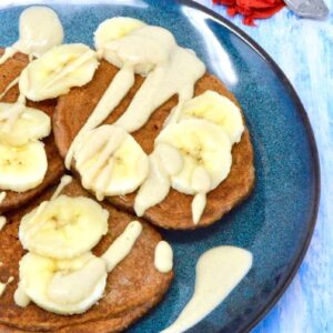 A dark blue plate piled with chocolate banana pancakes topped with sliced bananas and pear cashew cream.