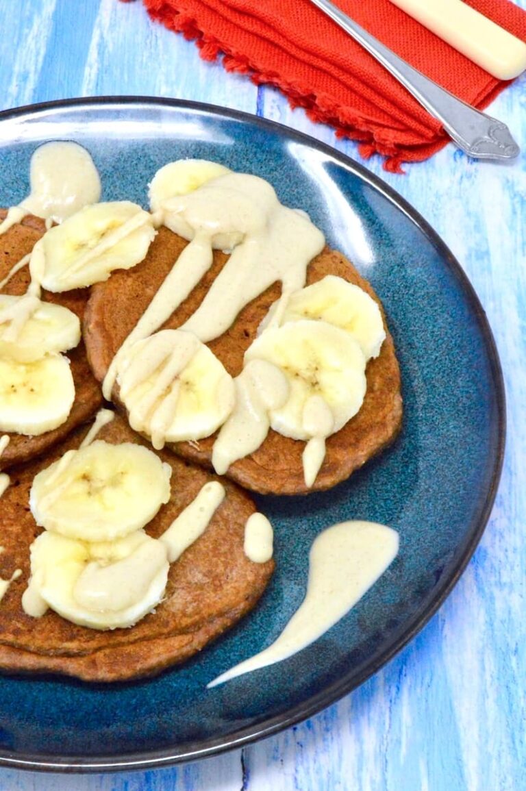 A dark blue plate piled with chocolate banana pancakes topped with sliced bananas and pear cashew cream.