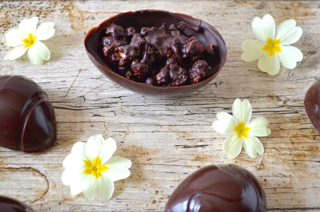 Homemade Easter eggs with dark chocolate salted caramel popcorn laid out on a table with primrose flowers.