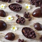 Homemade Easter eggs with dark chocolate salted caramel popcorn laid out on a table with primrose flowers.