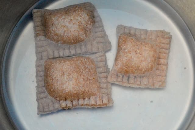 Homemade whole wheat ravioli simmering in a pan of salted water.