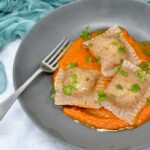 Homemade vegan ravioli on bed of tomato sauce with chopped parsley scattered over top.
