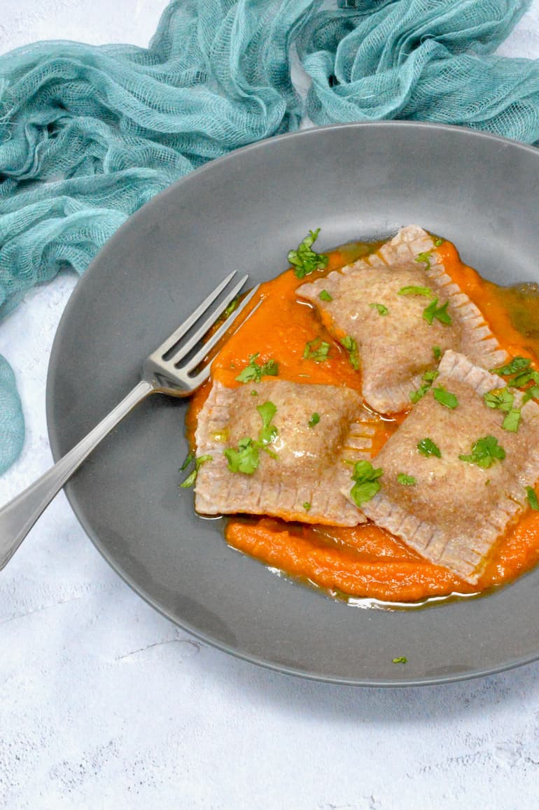 Homemade vegan ravioli on bed of tomato sauce with chopped parsley scattered over top.