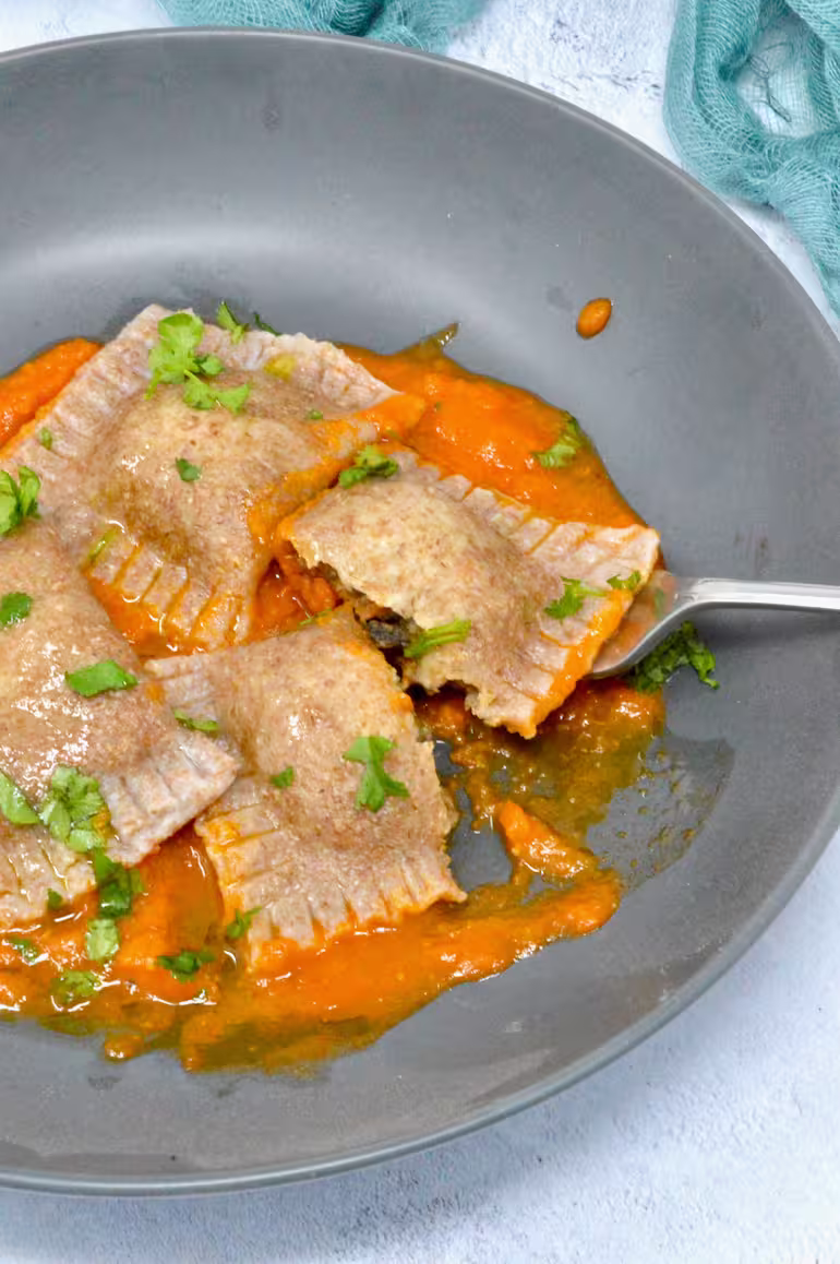 Homemade vegan ravioli on bed of tomato sauce with drizzle of olive oil and chopped parsley.