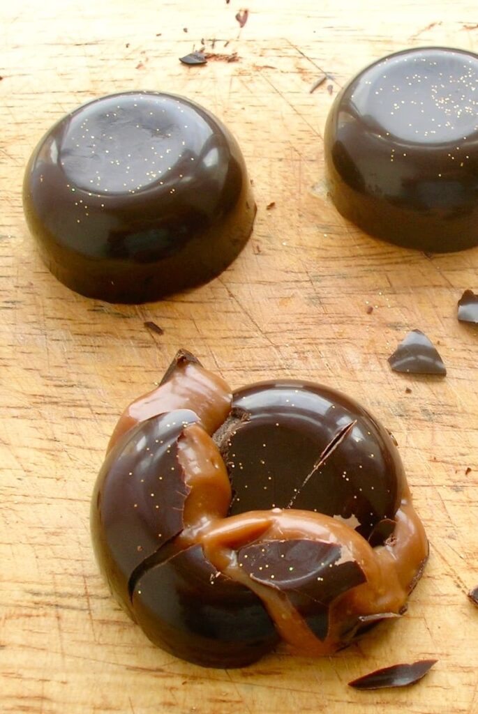 A purposefully cracked homemade passionfruit caramel chocolate with two whole ones above.