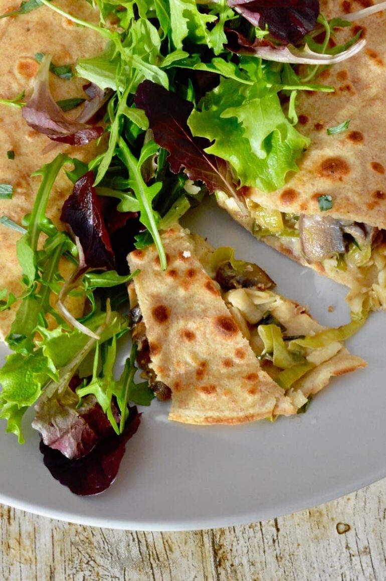 Savoury pancakes on a plate showing the leek and mushroom filling. A few salad leaves are on top of the pancakes.