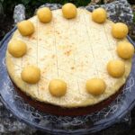 A traditional simnel cake with eleven marzipan apostles on a glass cake stand.