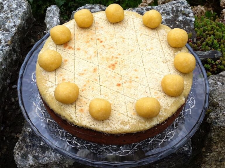 A traditional simnel cake with eleven marzipan apostles on a glass cake stand.
