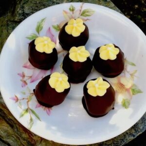 Six St Clement's cake truffles sitting on a saucer with yellow flowers stuck on top.
