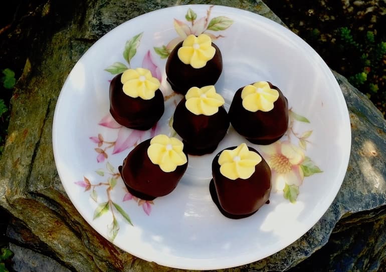 Six St Clement's cake truffles sitting on a saucer with yellow flowers stuck on top.