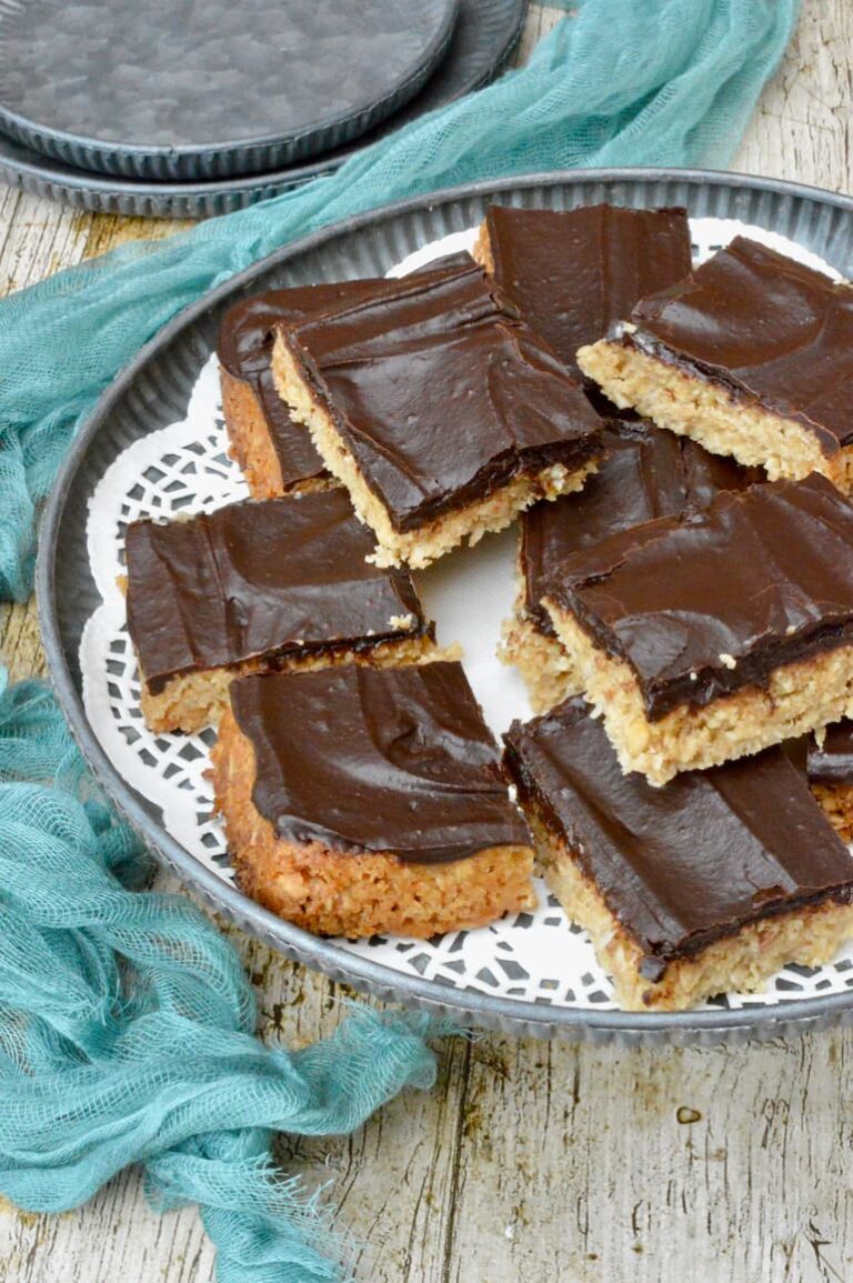 Chocolate topped vegan coconut flapjacks piled on doily lined grey platter.