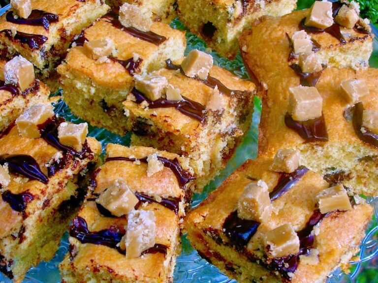 A close up of slices of choc chip fudge traybake drizzled with melted chocolate and topped with fudge pieces.