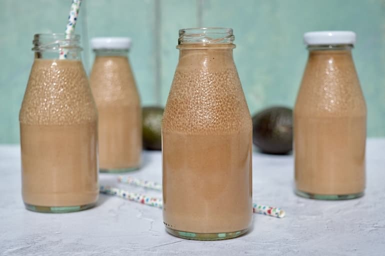Four bottles of chocolate avocado smoothies. Two with caps on and one with a straw.