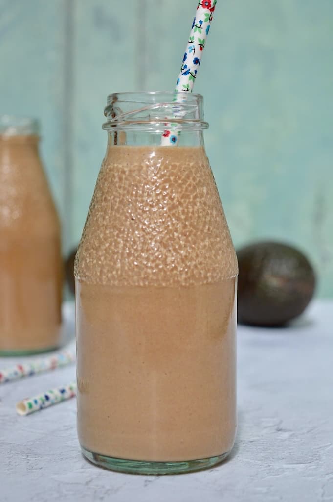 Chocolate avocado smoothie in a bottle with paper straw.