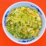 A blue side dish bowl of vegan stir-fried Brussels sprouts and leeks on an orange background.