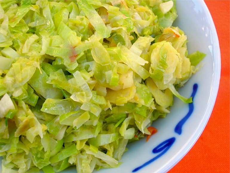 Stir-fried Brussels sprouts and leeks in a blue bowl with an orange background.