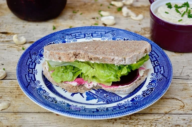 Vegan 'Cream Cheese', Spiced Pickled Beetroot & Lettuce Sandwich on a blue plate. Cashew nuts and other paraphernalia in the background.