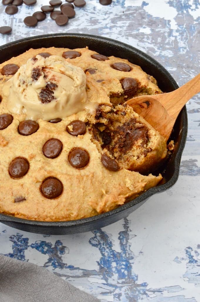 A giant vegan chocolate chip skillet cookie with a scoop of chocolate ice-cream on top.