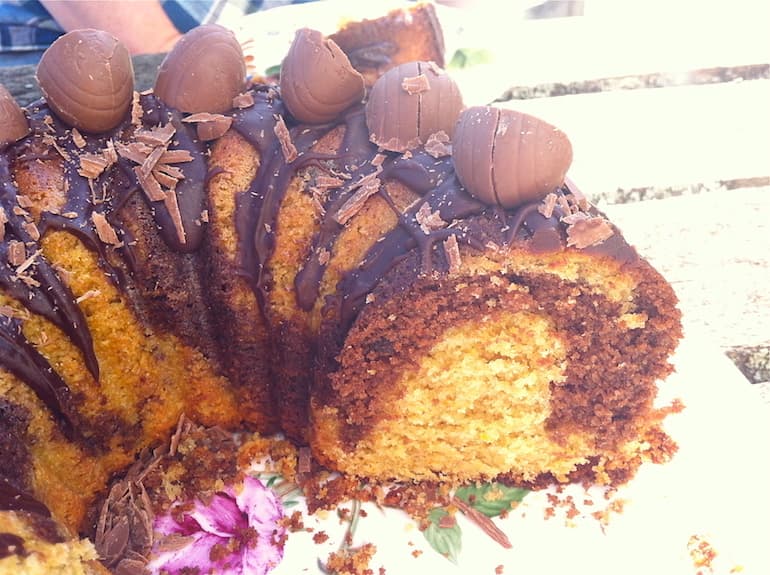 A cut through section of a spiced chocolate & orange Easter bundt cake drizzled with chocolate sauce and decorated with mini Easter eggs.