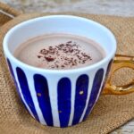 A blue stripy mug of gingerbread hot chocolate with chocolate sprinkles on top.